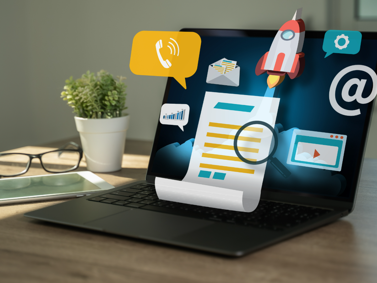 A laptop on a desk with content, email, video and analytics icons rising from the screen